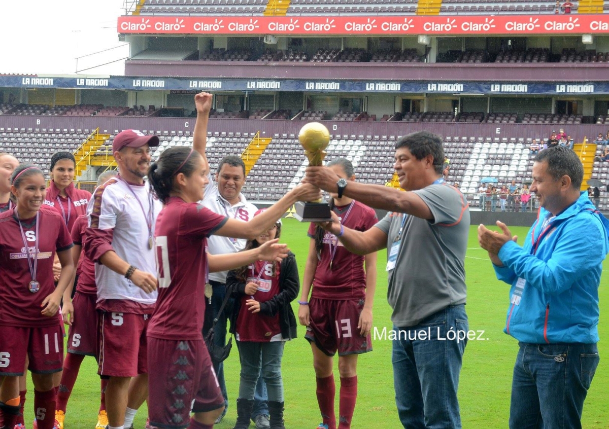 Katherine Alvarado (izquierda), capitana del Saprissa, recibe el trofeo de monarca del Campeonato Nacional de la Primera División 2015. Lo entrega Víctor Hugo Alfaro (segundo, de derecha a izquierda), presidente de la Liga de Fútbol Femenino, junto al jerarca de la Fedefútbol, Rodolfo Villalobos (foto Manuel López).